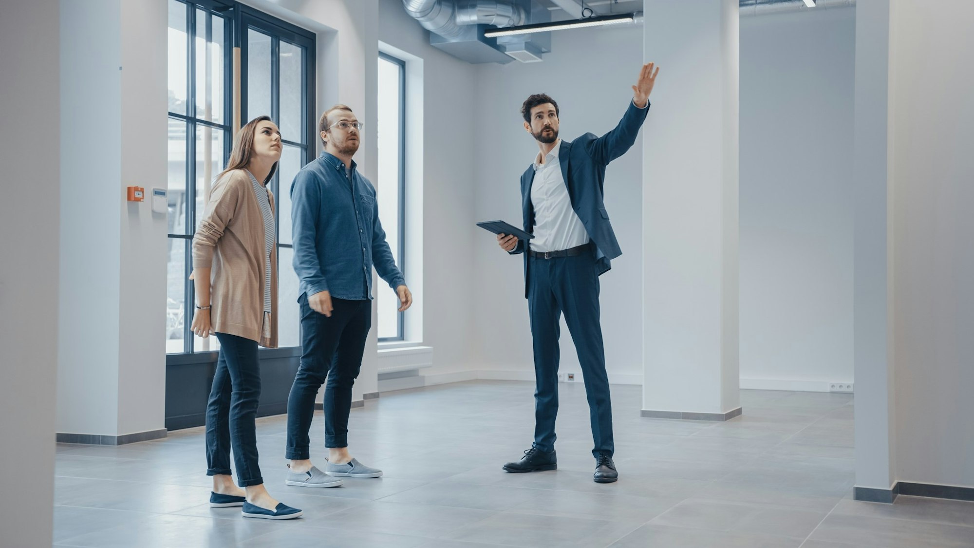 Three people in a modern office setting, one gesturing and possibly explaining something.