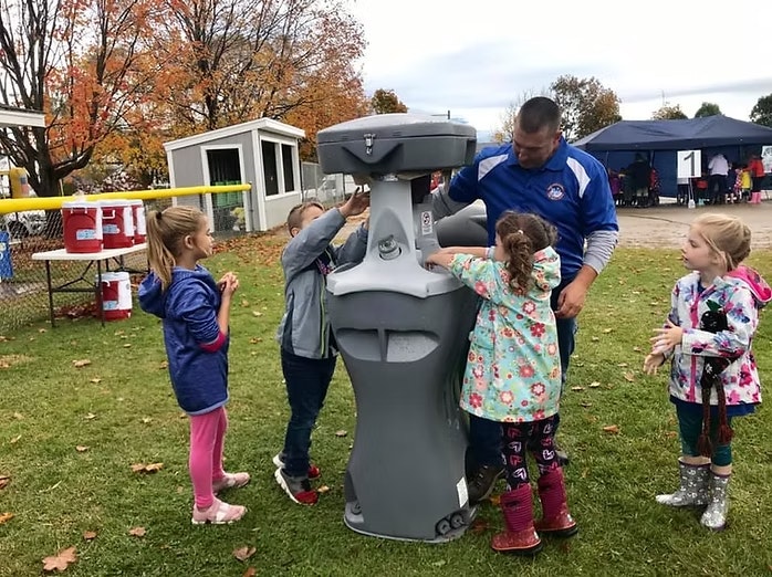 People using a portable handwashing station outdoors.