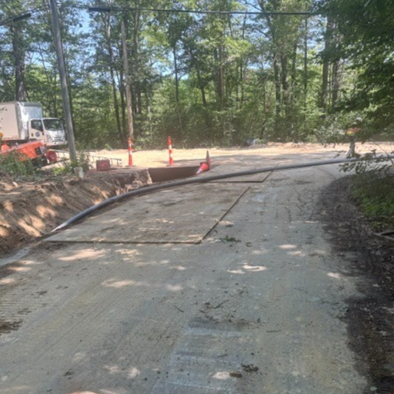The image shows a construction site with dirt, a road, a funnel, safety cones, and machinery surrounded by trees.