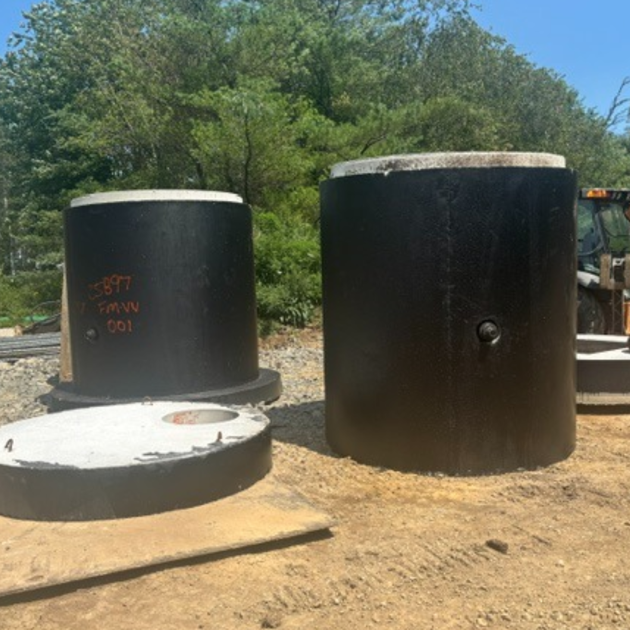 The image shows several large black cylindrical structures, likely storage tanks or chambers, sitting on a gravel surface in a natural setting.