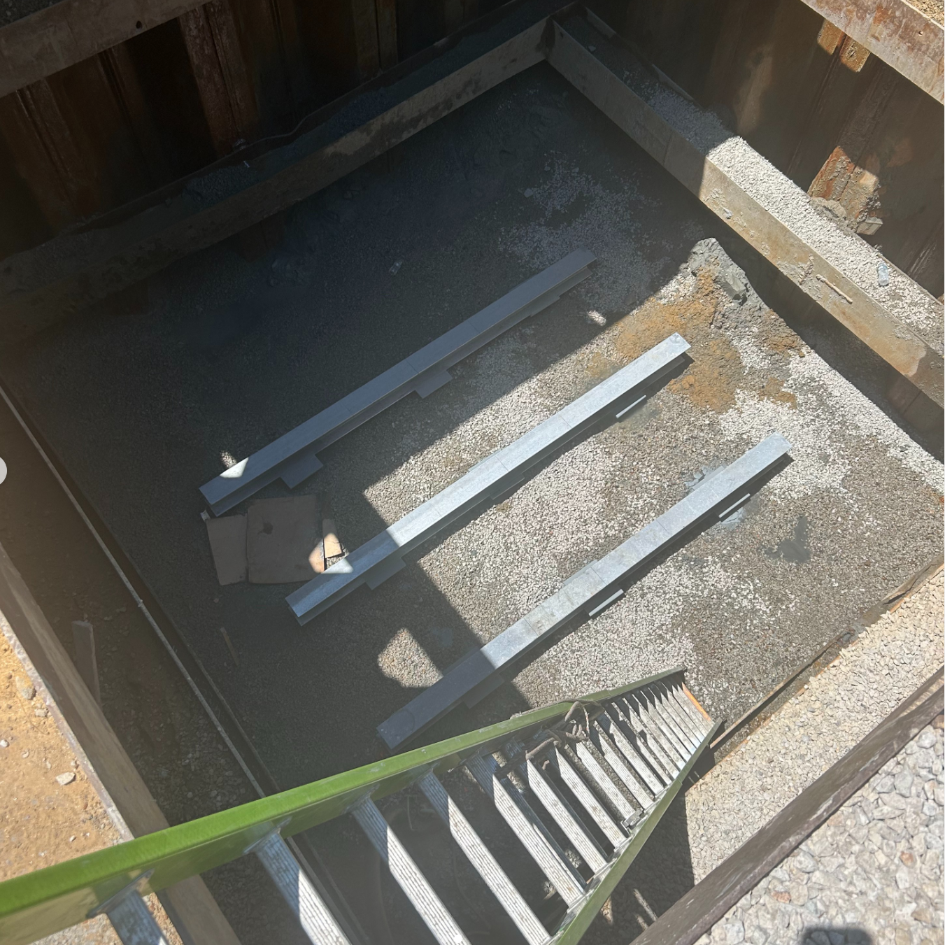 The image shows a construction site with steps leading down to a pit containing gravel and metal beams.