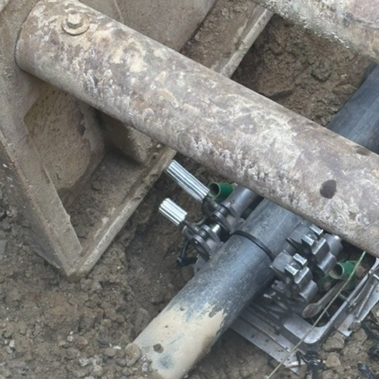 The image shows industrial machinery components, including pipes and connectors, set in a dirt excavation site.