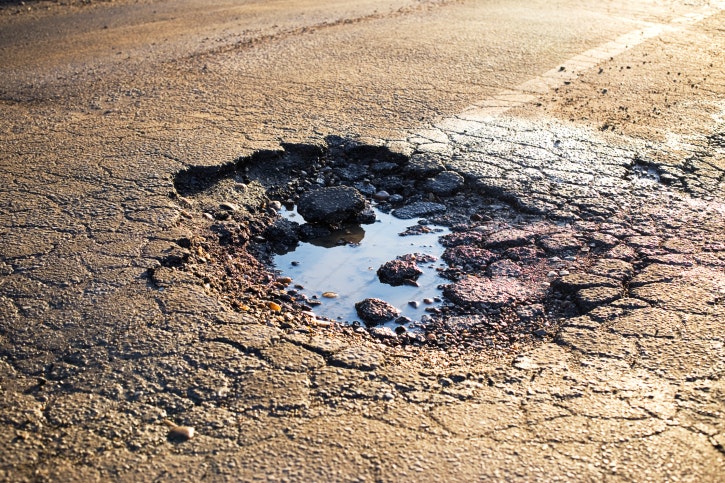 A pothole filled with water on a cracked asphalt road.