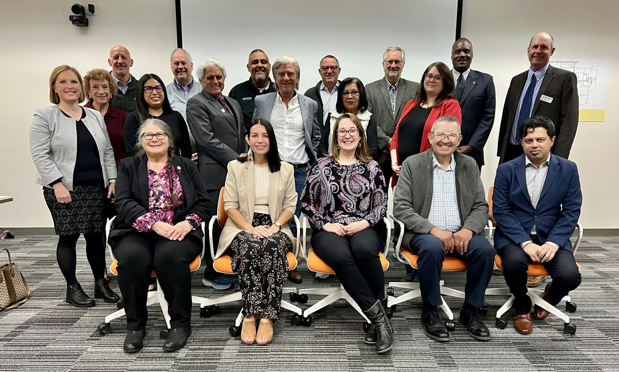 A group of 18 people, some seated and some standing, posing for a photo indoors.
