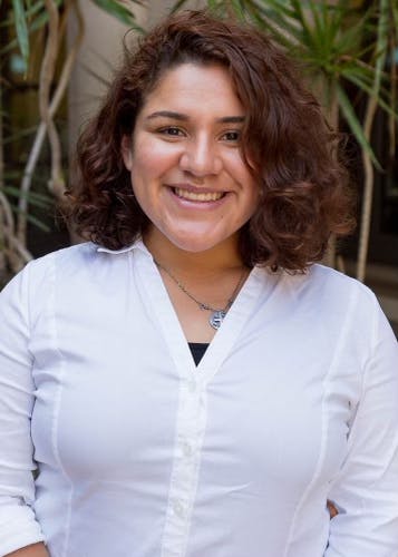A smiling person with curly hair in a white shirt.