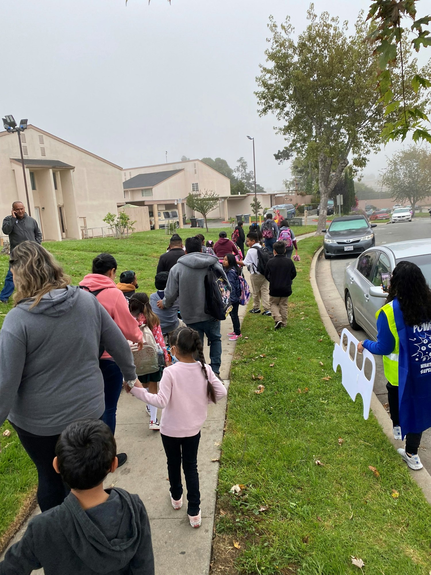 Adults and children walking along the sidewalk to school