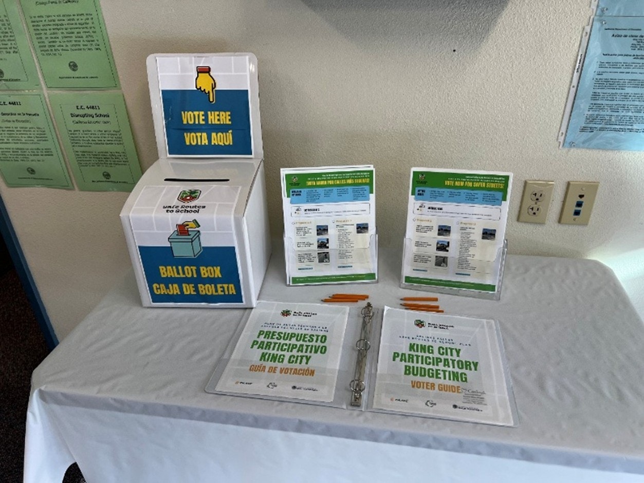 Ballot box setup for voting with guides and materials in English and Spanish for King City's participatory budgeting.