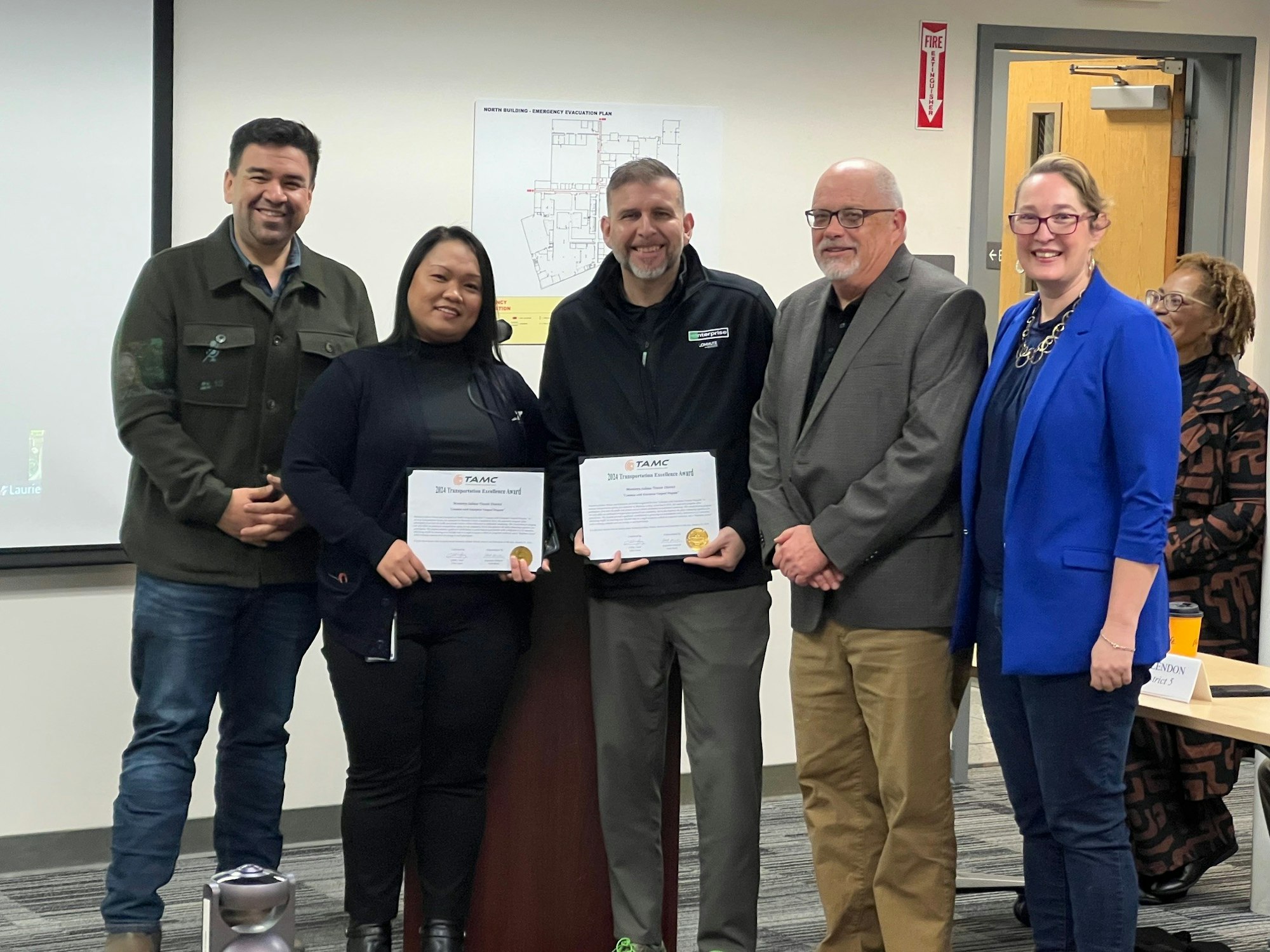 A group of five people posing with certificates of recognition, indoors.
