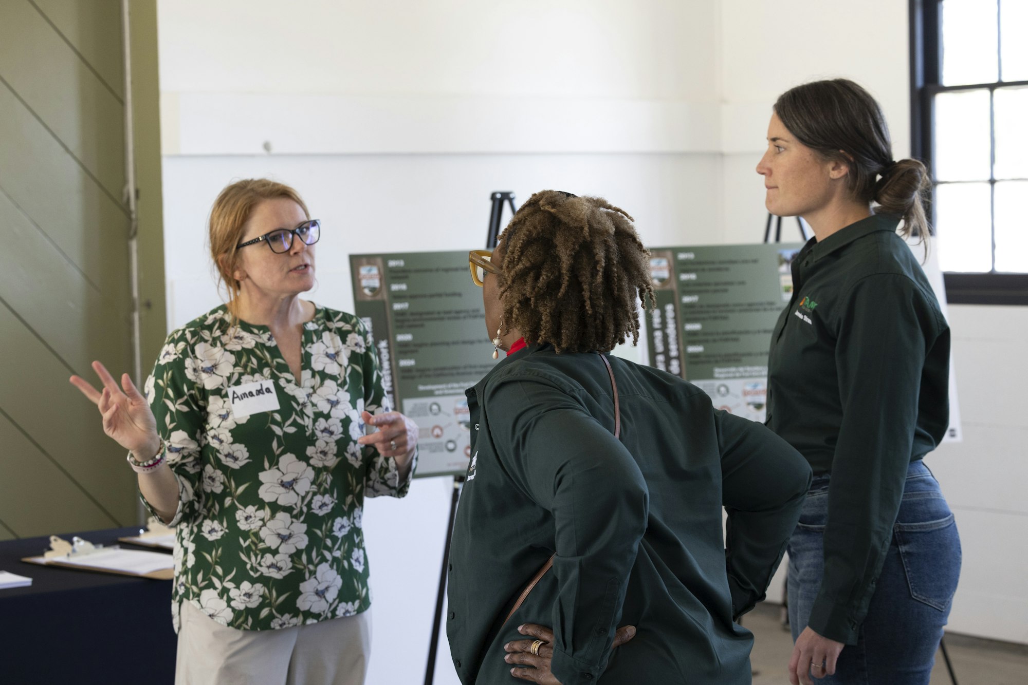 Three people are engaged in a discussion in front of display boards with information.