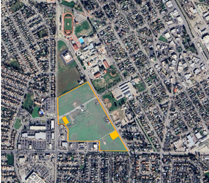 Aerial view of a city area with a highlighted zone, sports fields, buildings, roads, and dense housing.