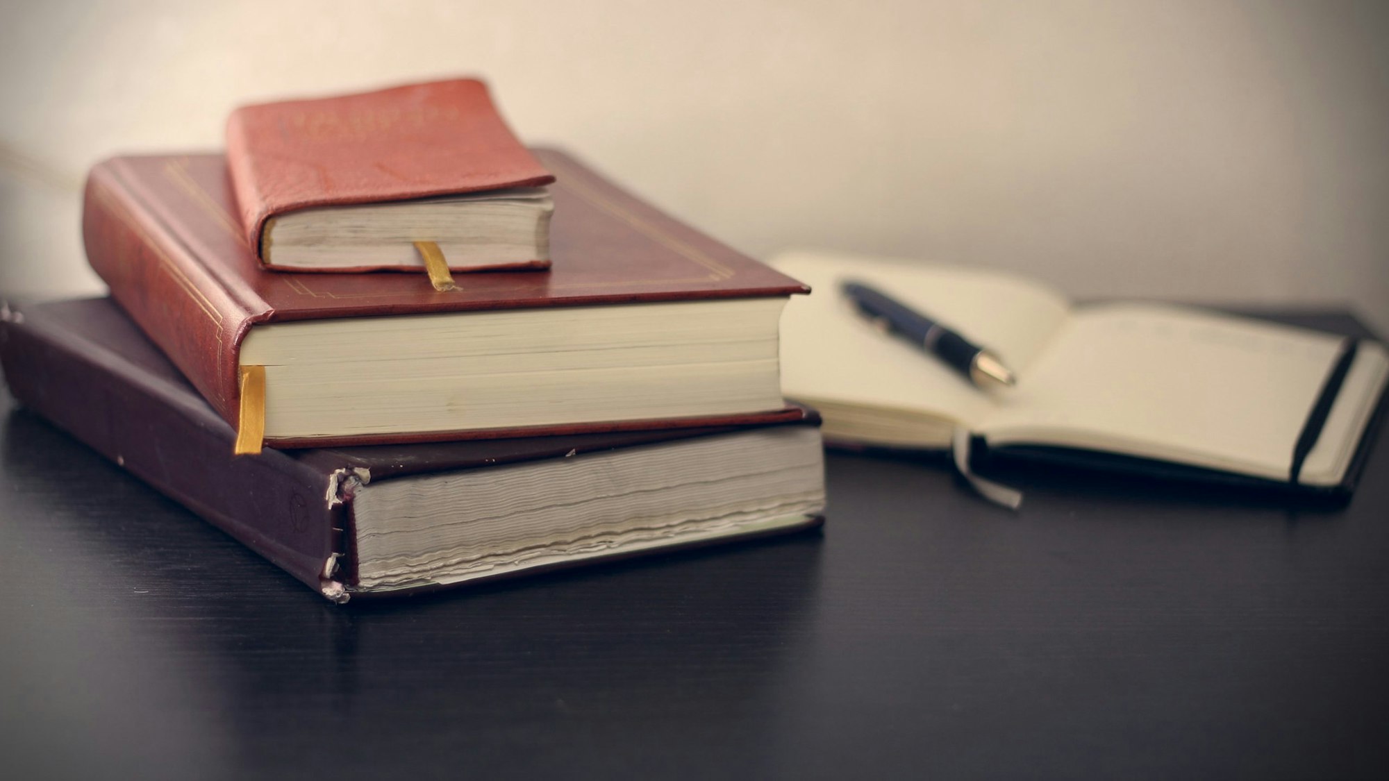 Stack of books and an open notebook with a pen on a dark desk.