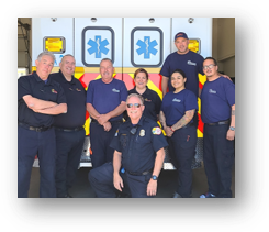 A group of eight people, some in uniform, posing in front of an ambulance.