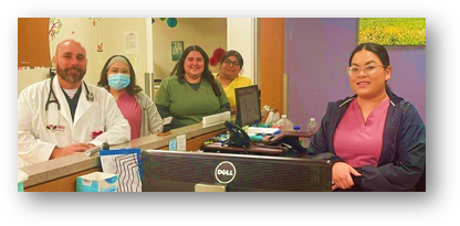 A group of five medical professionals poses behind a reception desk, some in scrubs and one in a white coat with a stethoscope.