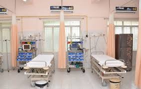 The image shows a hospital ward with multiple hospital beds, medical equipment, and curtains for privacy.