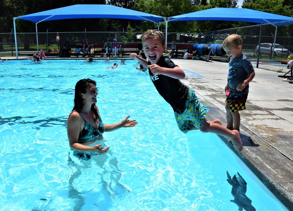 May contain: summer, leisure activities, person, sport, swimming, water, water sports, pool, face, head, photography, portrait, clothing, shorts, swimming pool, swimwear, boy, child, male, adult, female, woman, lifejacket, vest, plant, potted plant, architecture, building, outdoors, and shelter