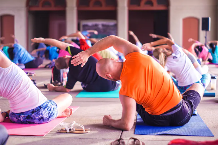 A group of people participating in a yoga class, performing stretches on colorful mats in a spacious setting.