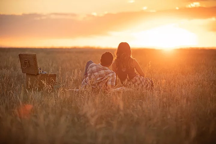 Two people sitting in a field at sunset with a picnic basket.