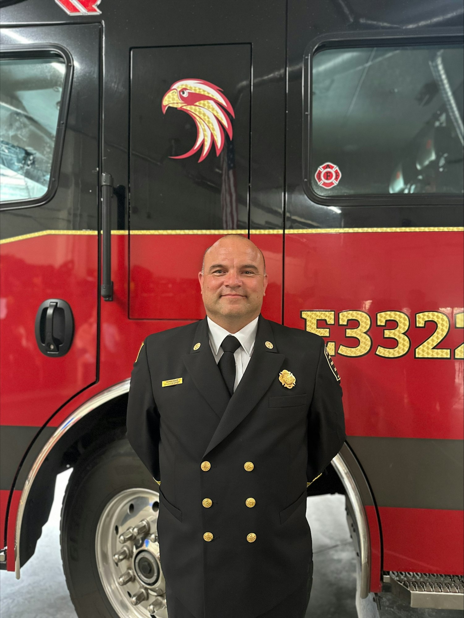 A person in firefighter dress uniform standing in front of a fire truck.
