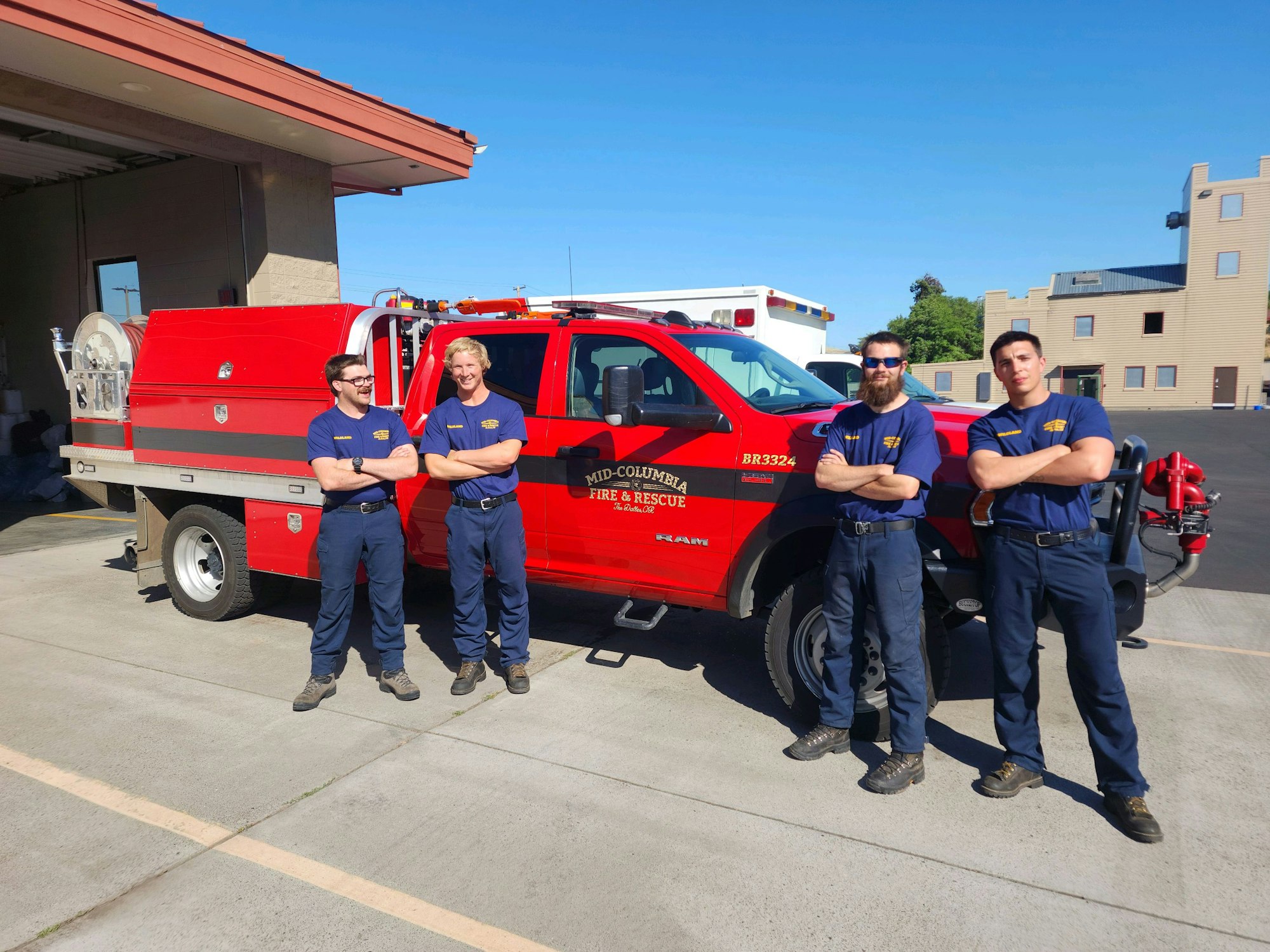 Four firefighters standing proudly in front of a red fire rescue vehicle.