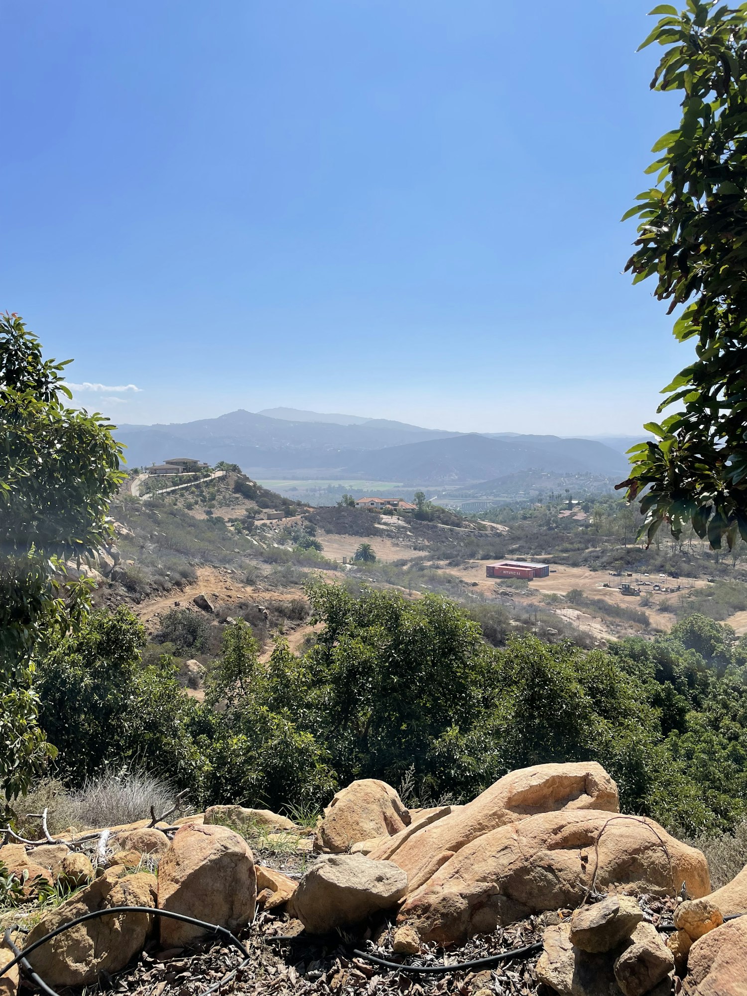 Rocky hillside with vegetation, clear blue sky and valley in the distance. (Note: Image is rotated 90 degrees clockwise)