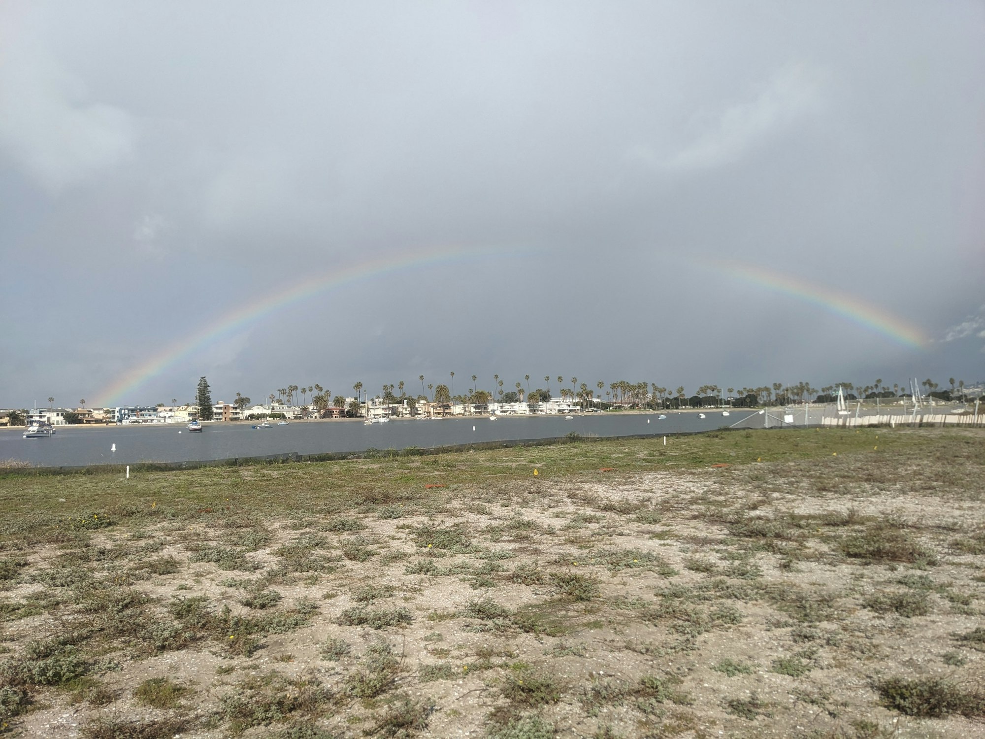 A rainbow arcs over a waterfront landscape with cloudy skies.