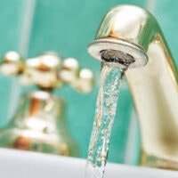 A close-up of water flowing from a gold-colored tap.