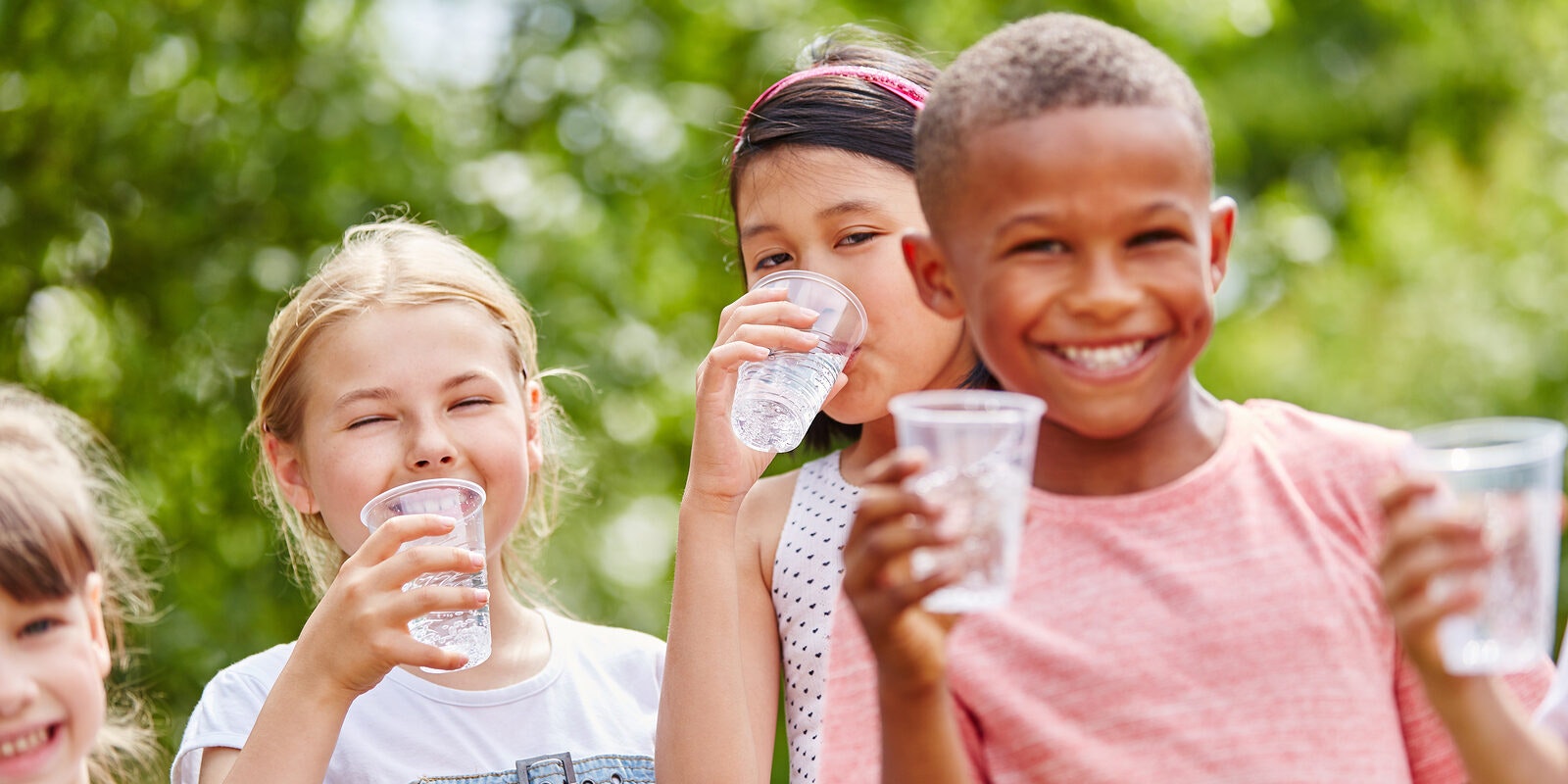 Group of smiling children drinking water outdoors.