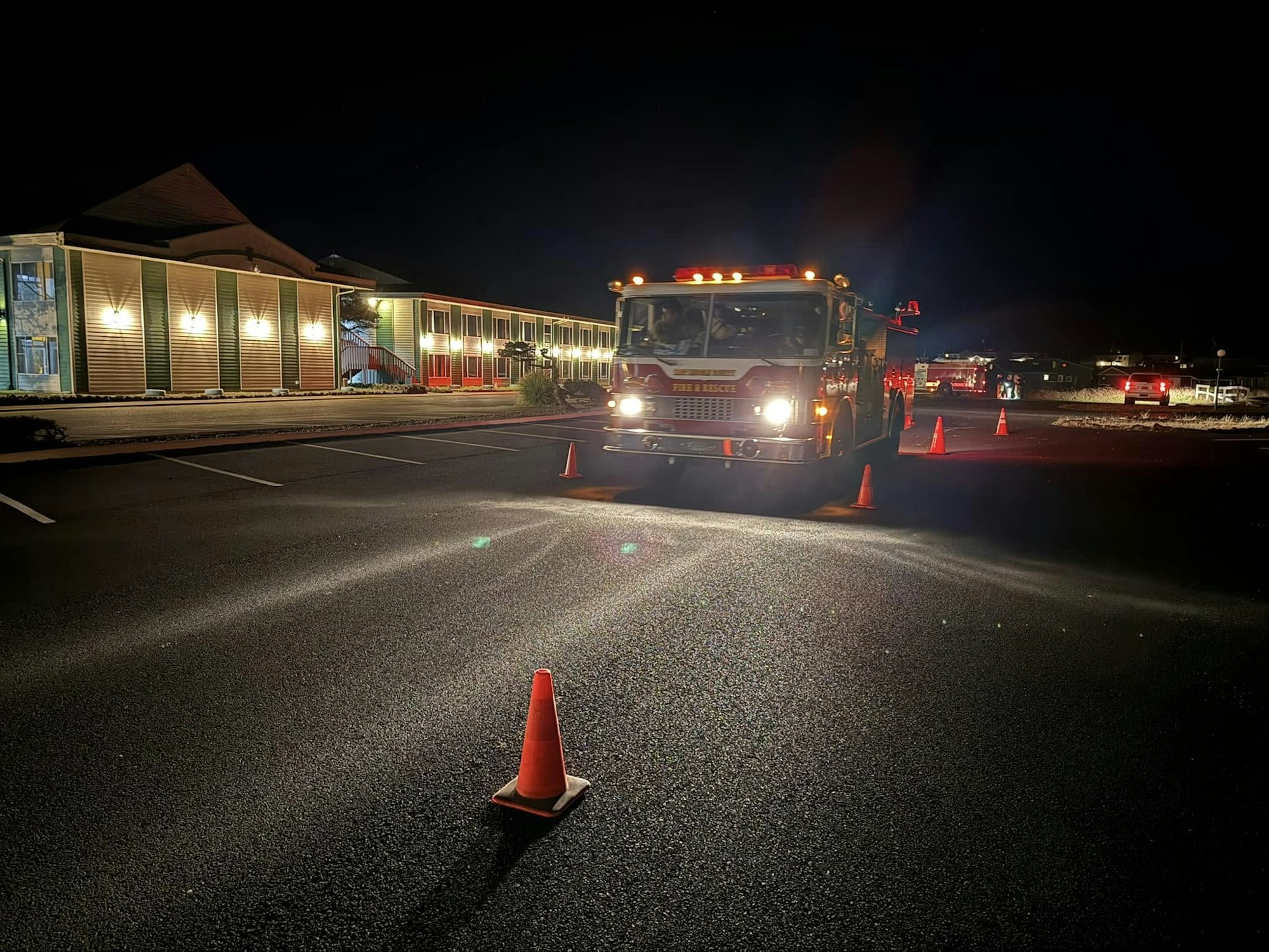 Fire truck at night on a road with cones, near a building.
