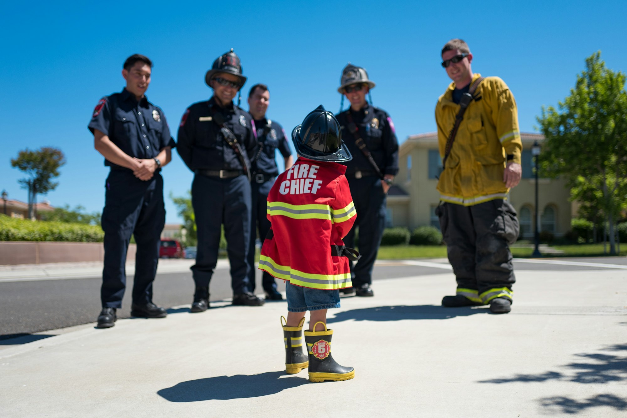 A child dressed as a "Fire Chief" stands proudly in front of several firefighters, showcasing a moment of admiration and inspiration.