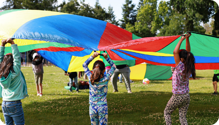 Children are playing with a colorful parachute in a park, enjoying outdoor activities together.