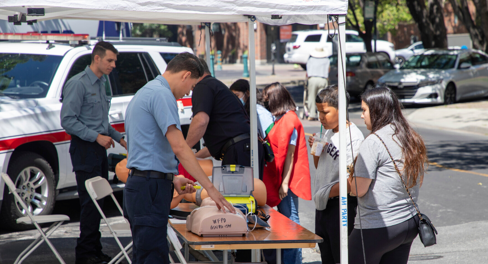 A first aid demonstration with people around a table, emergency vehicle in background at our 2022 health fair