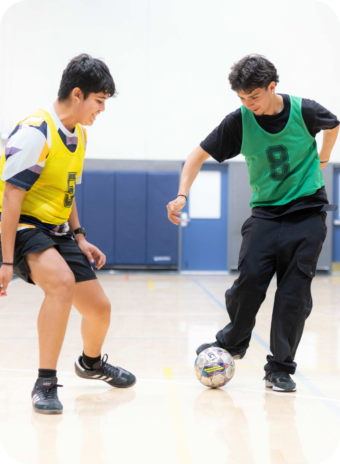 Two people in numbered jerseys play indoor soccer on a court.