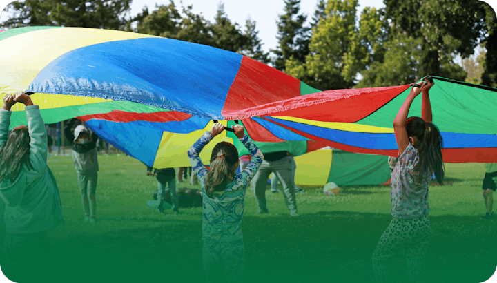 Children playing with a colorful parachute outdoors.