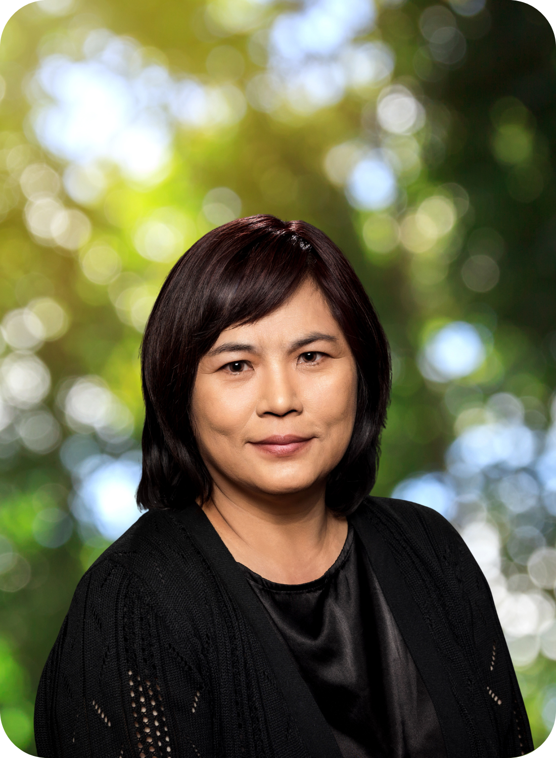 A person with short dark hair in a black outfit, set against a blurred natural background.