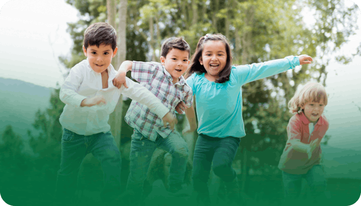 Four children happily running outdoors, surrounded by trees.