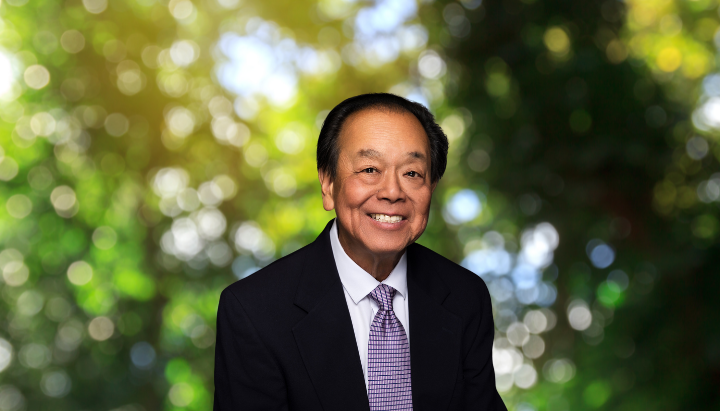A man in a suit smiling with a blurred nature background.