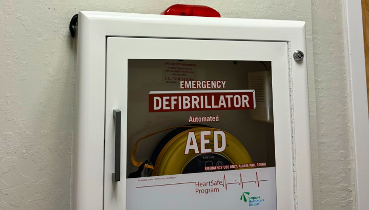 Wall-mounted automated external defibrillator (AED) in a white cabinet with an alarm and emergency instructions.