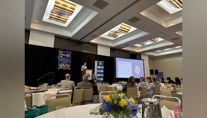 A conference room with attendees and a speaker presenting on "Depression in the U.S." at a Rotary Club event.