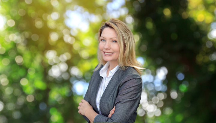 A person in formal attire smiling against a blurred, outdoor background.