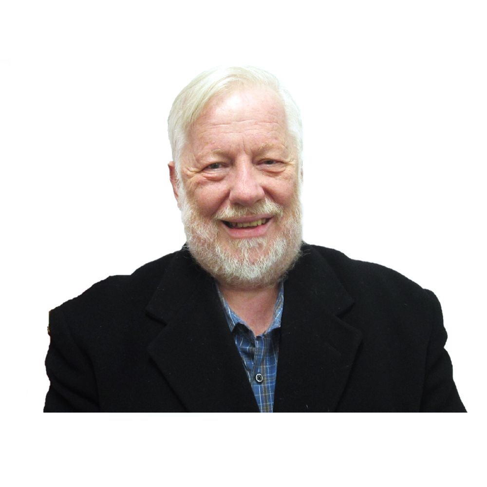 A smiling person with a light beard and light hair, wearing a black jacket over a checkered shirt.