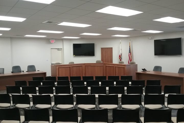 A spacious, modern meeting room with rows of chairs, a wooden podium, and a few screens, possibly for presentations or hearings.