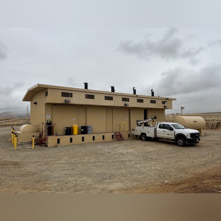 A utility building in a rural area with a parked white truck and large tanks nearby. Overcast sky.