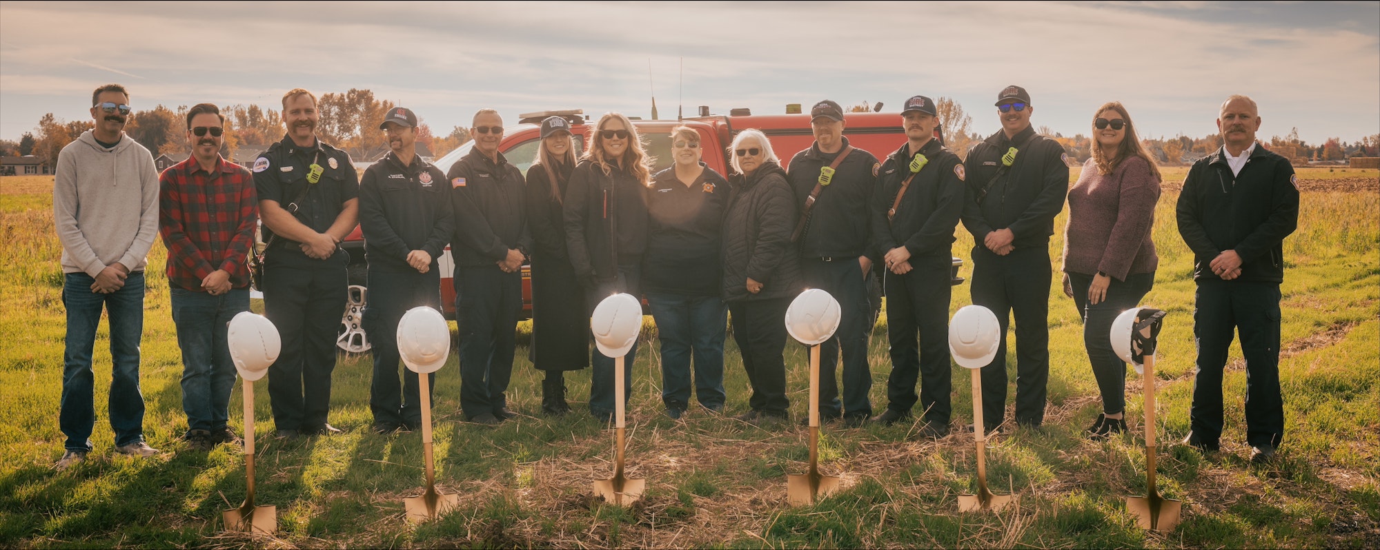 A group of people standing in a field with shovels and helmets, possibly at a groundbreaking event.
