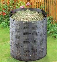 A black compost bin filled with organic matter, set in a garden with a wooden fence in the background.