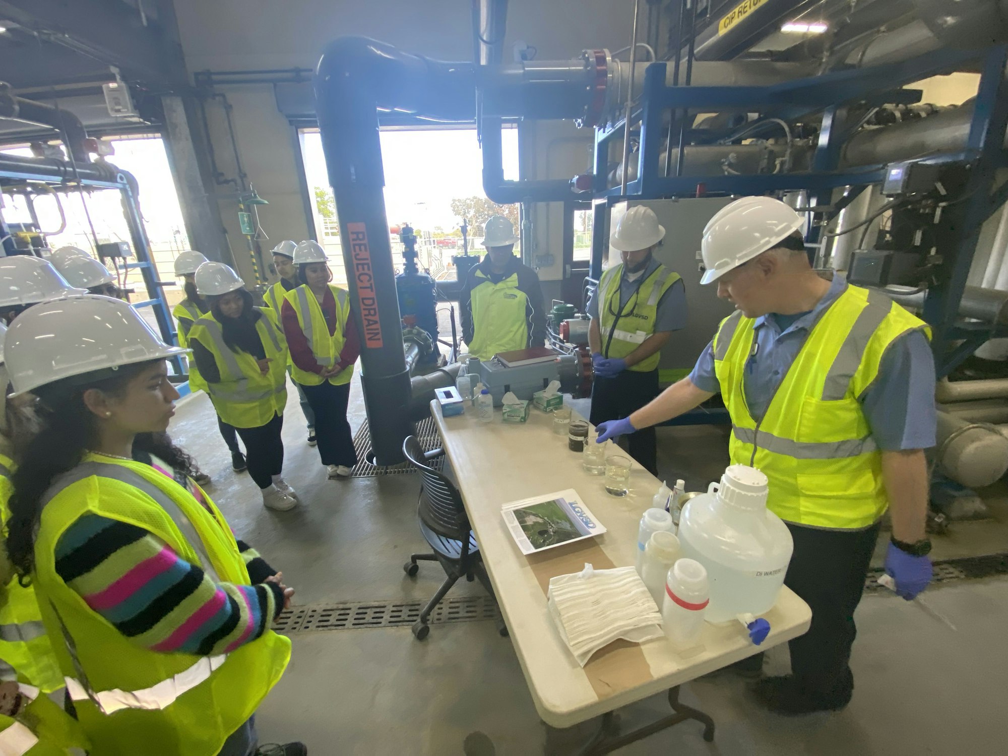 Group of people wearing hard hats and high-visibility vests in an industrial setting, possibly a training or tour.