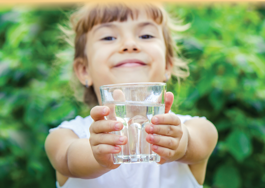 A smiling child holding a glass of water outdoors.