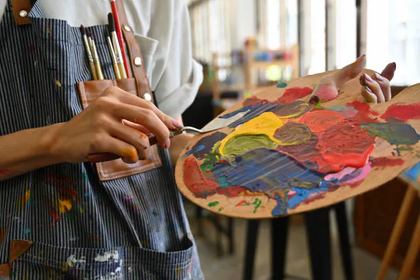 An artist holding a palette filled with vibrant paints, wearing an apron with brushes. Creative atmosphere in an art studio.