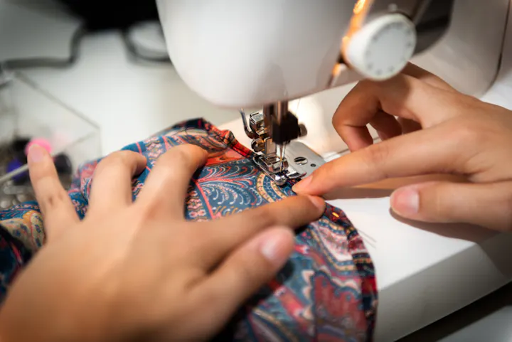 A person is sewing colorful fabric on a sewing machine, showcasing hands guiding the material.