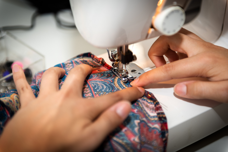 A person is sewing colorful fabric on a sewing machine, showcasing hands guiding the material.