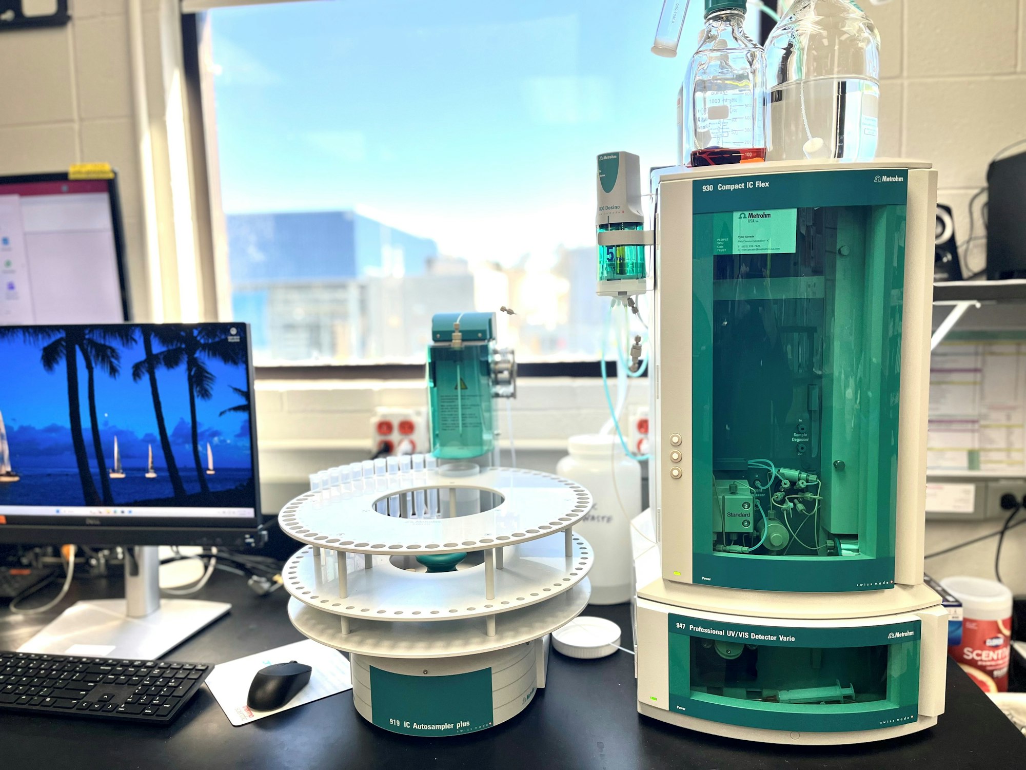 A lab setup with chromatography equipment, computer, and reagent bottles by a window.